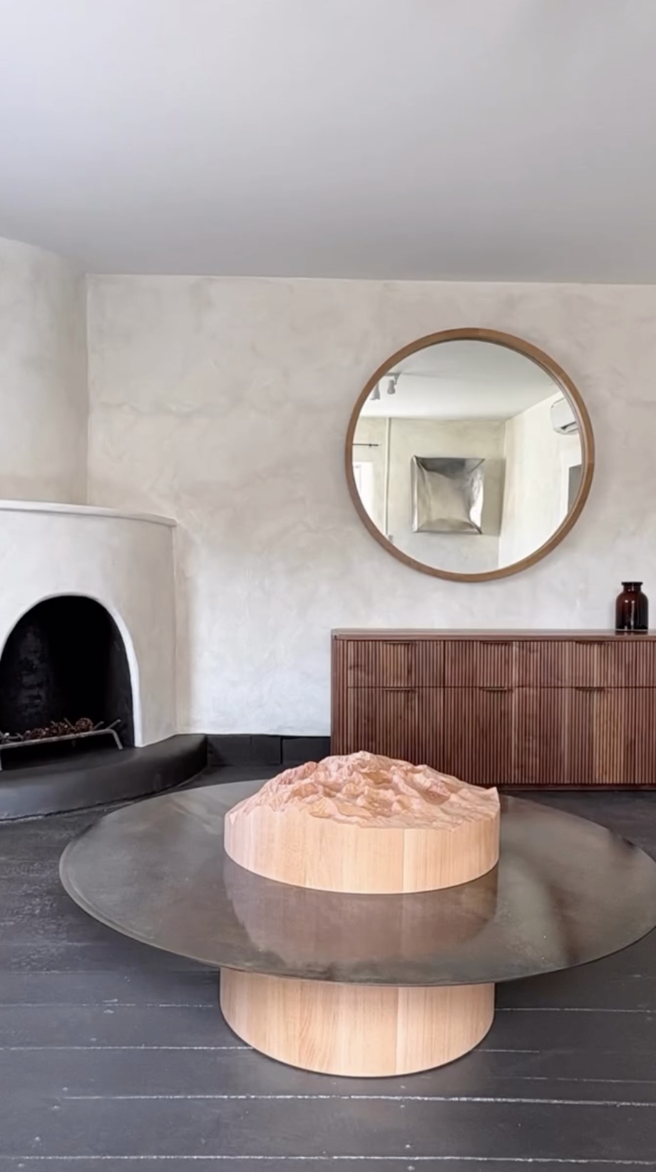 Gallery interior with a fireplace, round mirror, wood cabinet and sculptural table